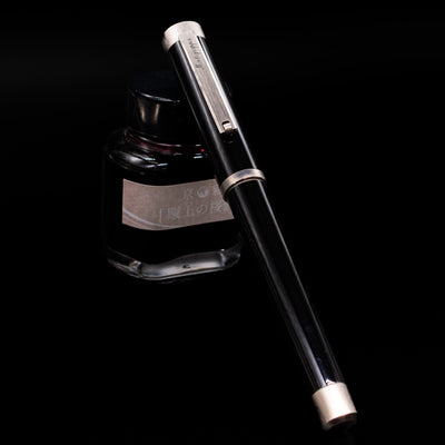 Montegrappa Zero Black & Palladium Fountain Pen - Preowned capped, leaning against an ink bottle. 
