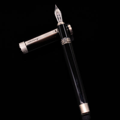 Montegrappa Zero Black & Palladium Fountain Pen - Preowned laying on top of its cap in a crossed position showing full view of the entire uncapped pen.
