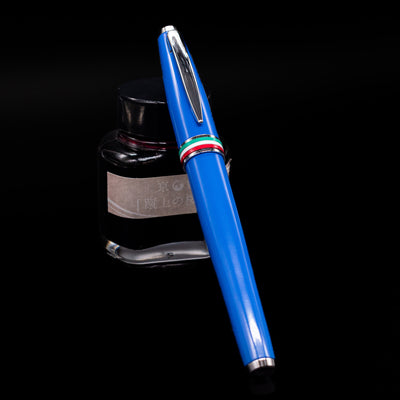 Monteverde Aldo Domani Italia Fountain Pen - Exotic Blue capped, leaning against an ink bottle. 