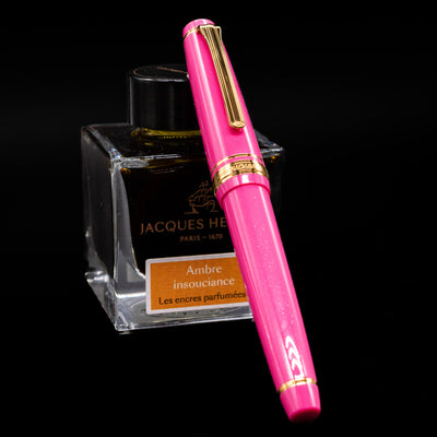 Nagasawa Original Fountain Pen - Suma-Rikyu Rose capped, leaning against an ink bottle. 