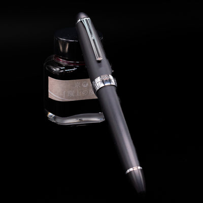 Nagasawa Original Large Fountain Pen - Black & Silver FL (For Lawyer) capped, leaning against an ink bottle. 