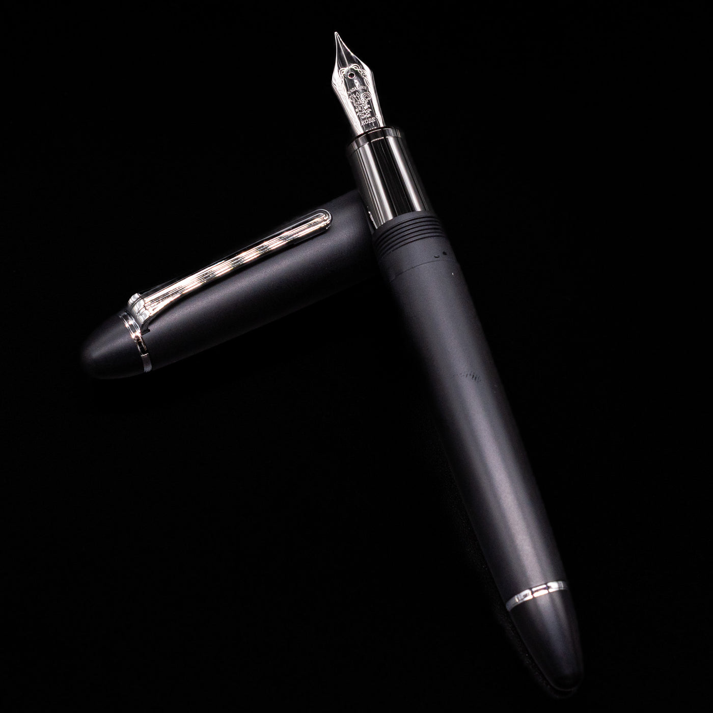 Nagasawa Original Large Fountain Pen - Black & Silver FL (For Lawyer) laying on top of its cap in a crossed position showing full view of the entire uncapped pen.