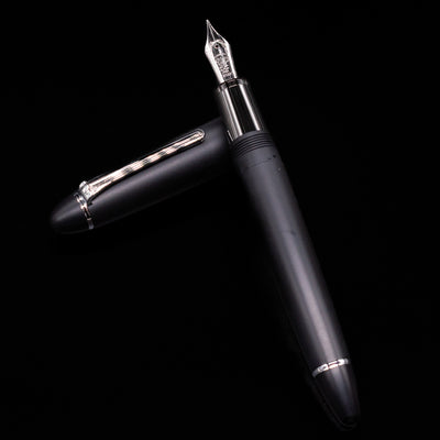 Nagasawa Original Large Fountain Pen - Black & Silver FL (For Lawyer) laying on top of its cap in a crossed position showing full view of the entire uncapped pen.