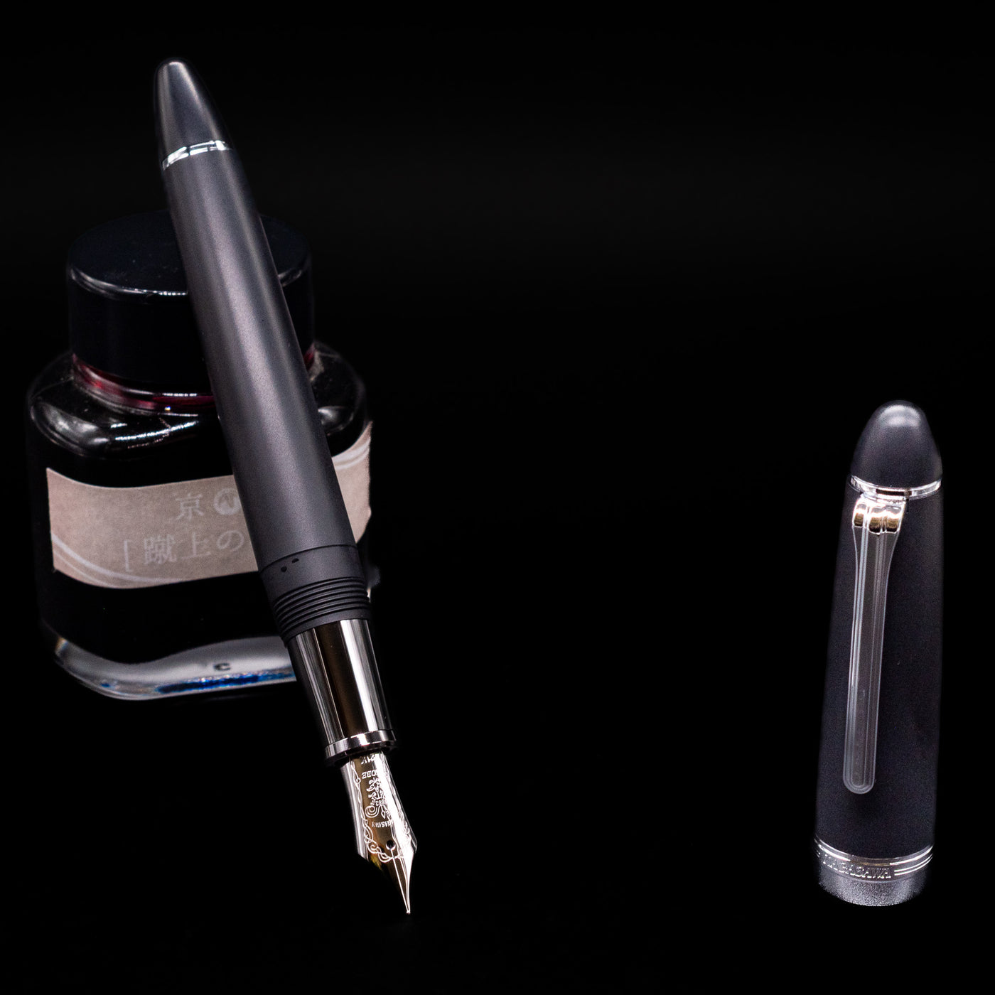 Nagasawa Original Large Fountain Pen - Black & Silver FL (For Lawyer) leaning on an ink bottle uncapped showcasing the detailing on the nib.