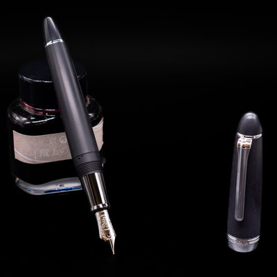 Nagasawa Original Large Fountain Pen - Black & Silver FL (For Lawyer) leaning on an ink bottle uncapped showcasing the detailing on the nib.