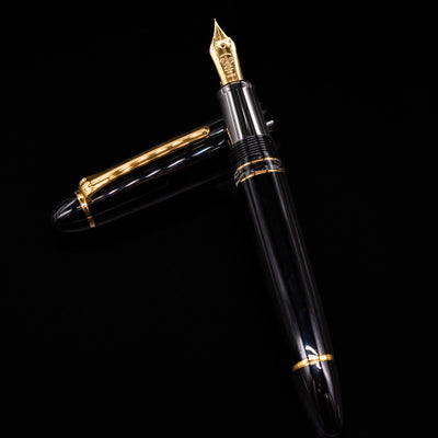 Nagasawa Original Large Piston Fountain Pen - Realo FL (For Lawyer)  laying on top of its cap in a crossed position showing full view of the entire uncapped pen.