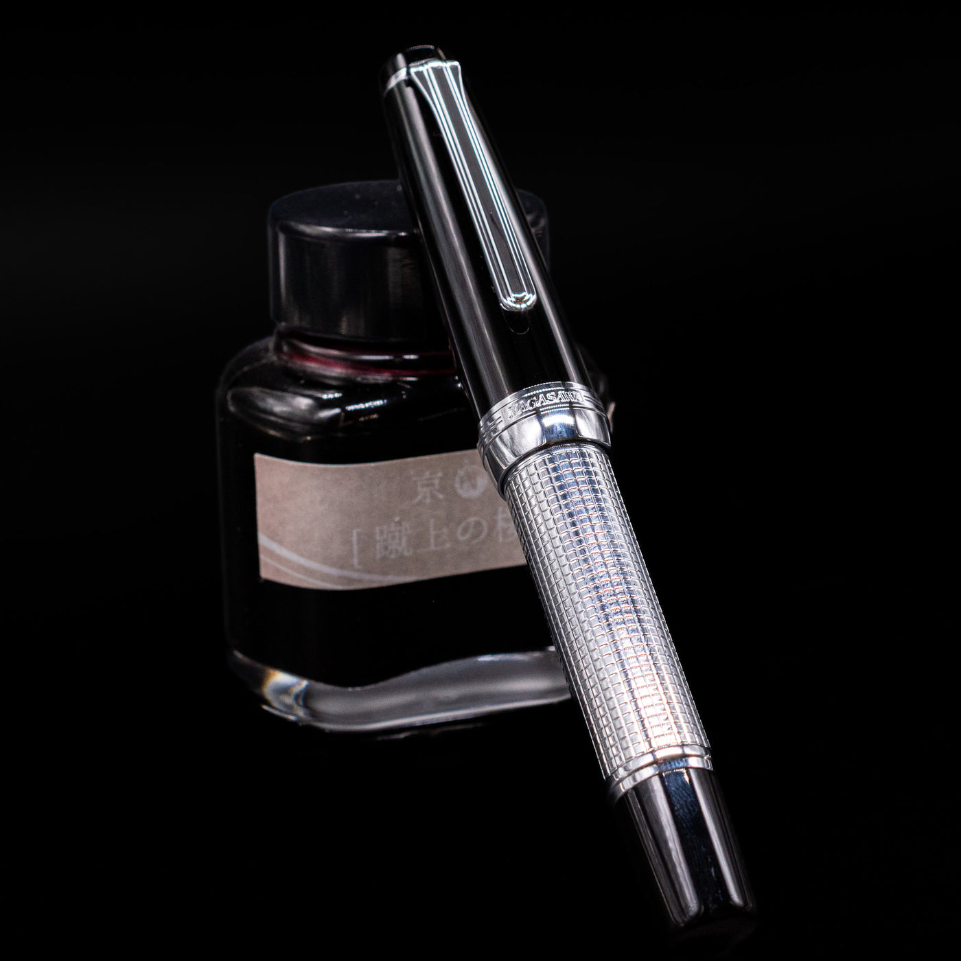 Nagasawa Original Limited Edition Fountain Pen - Engrave Kou capped, leaning against an ink bottle. 