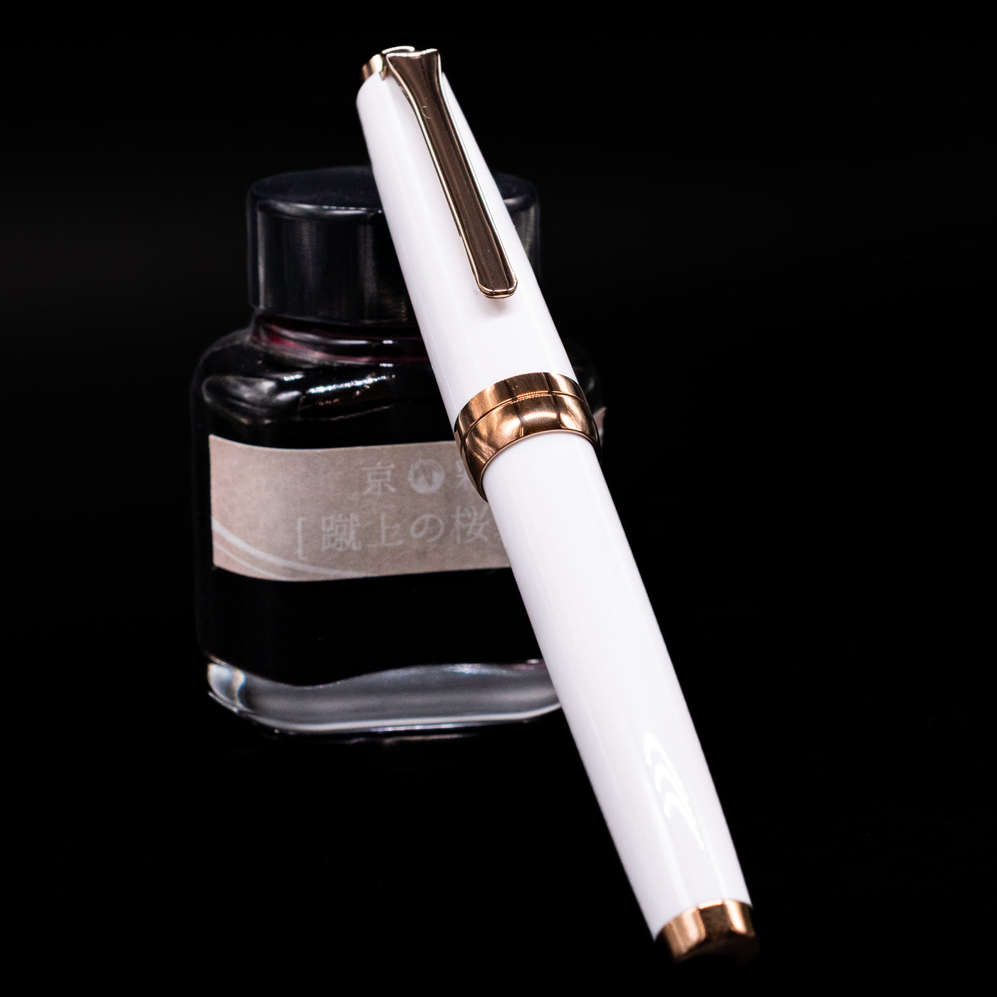 Nagasawa Original Limited Edition Fountain Pen - Odyssey Snow White  capped, leaning against an ink bottle. 