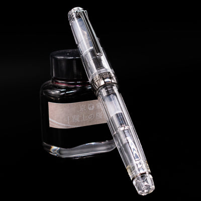 Nagasawa Original Professional Gear Fountain Pen - Skeleton Black capped, leaning against an ink bottle. 