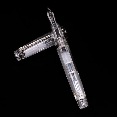 Nagasawa Original Professional Gear Fountain Pen - Skeleton Black laying on top of its cap in a crossed position showing full view of the entire uncapped pen.
