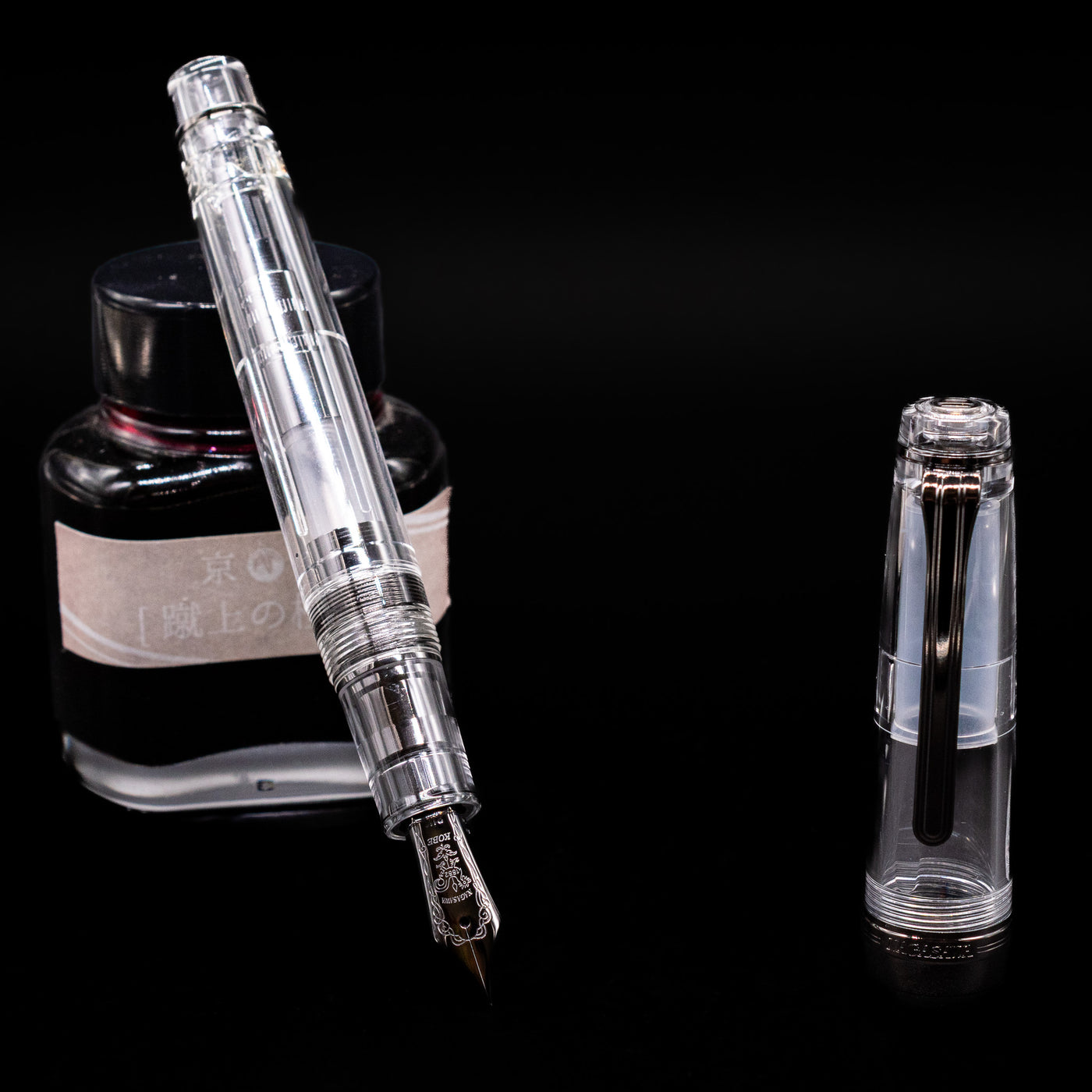 Nagasawa Original Professional Gear Fountain Pen - Skeleton Black leaning on an ink bottle uncapped showcasing the detailing on the nib.