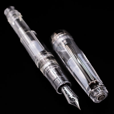 A full view of the Nagasawa Original Professional Gear Fountain Pen - Skeleton Black uncapped, with its cap laying next to the pen. 