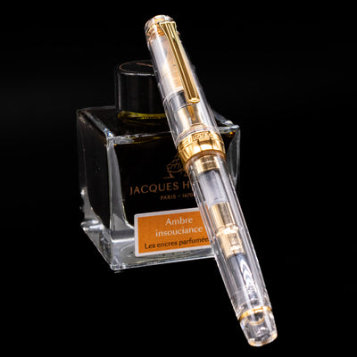 Nagasawa Original Professional Gear Fountain Pen - Skeleton Gold capped, leaning against an ink bottle. 