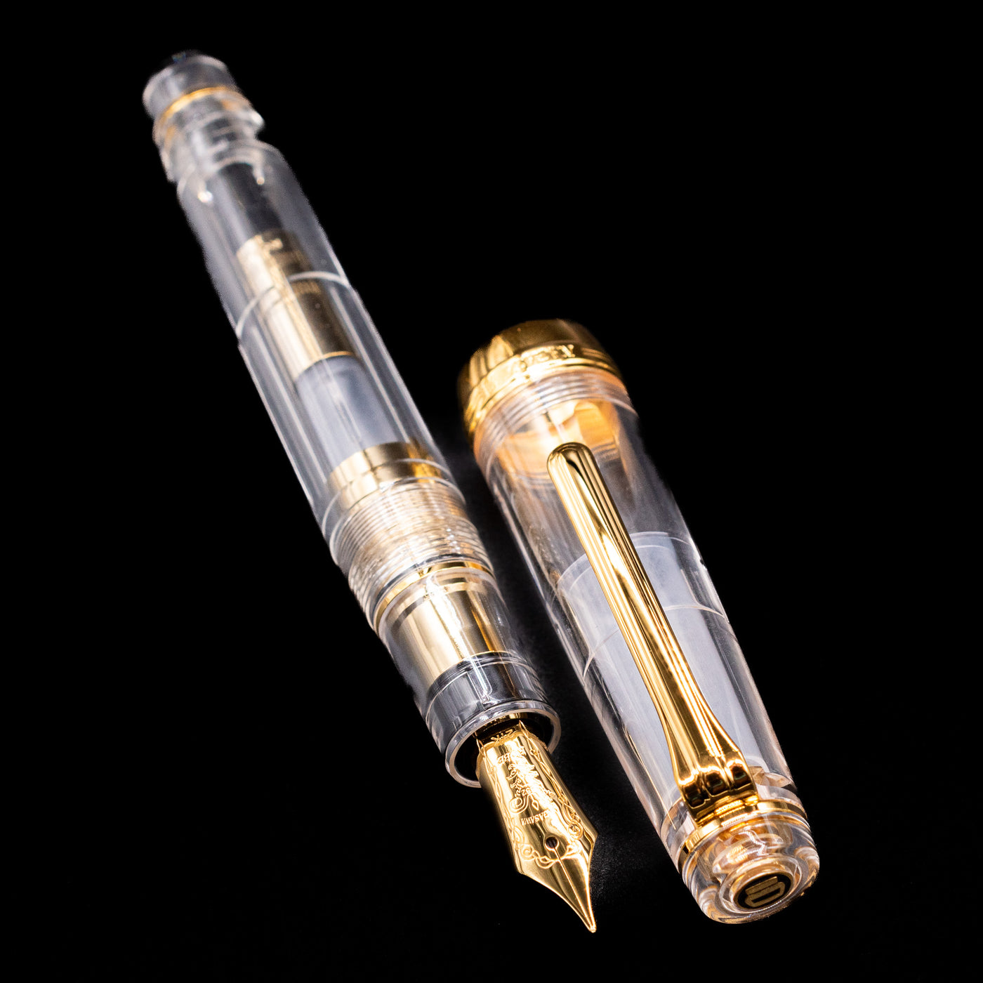 A full view of the Nagasawa Original Professional Gear Fountain Pen - Skeleton Gold uncapped, with its cap laying next to the pen. 