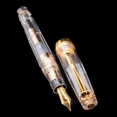 A full view of the Nagasawa Original Professional Gear Fountain Pen - Skeleton Gold uncapped, with its cap laying next to the pen. 