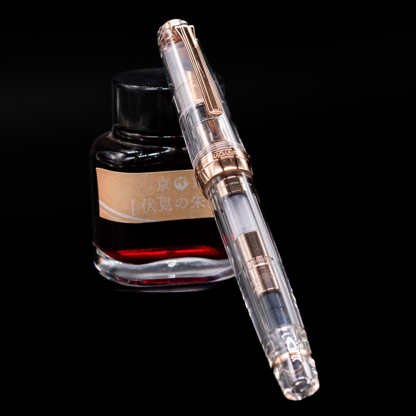 Nagasawa Original Professional Gear Fountain Pen - Skeleton Pink Goldc apped, leaning against an ink bottle. 