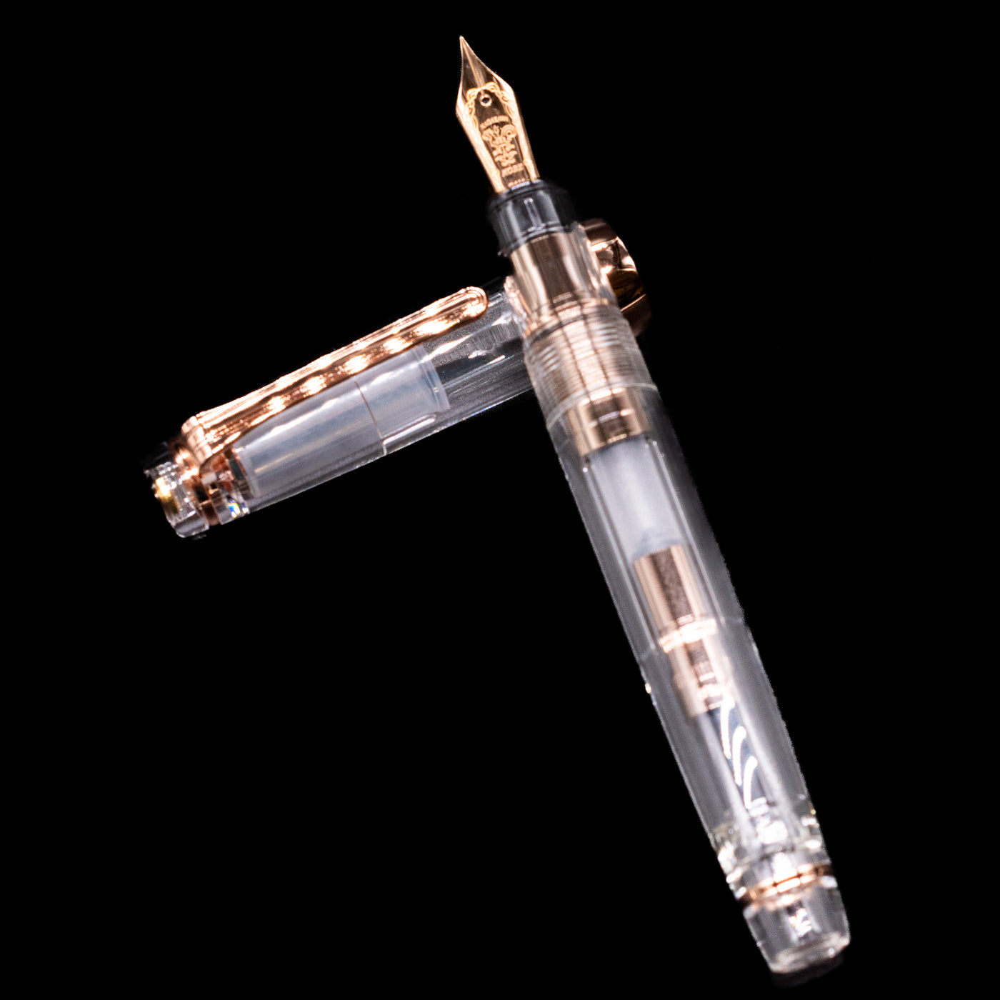 Nagasawa Original Professional Gear Fountain Pen - Skeleton Pink  laying on top of its cap in a crossed position showing full view of the entire uncapped pen.Gold.