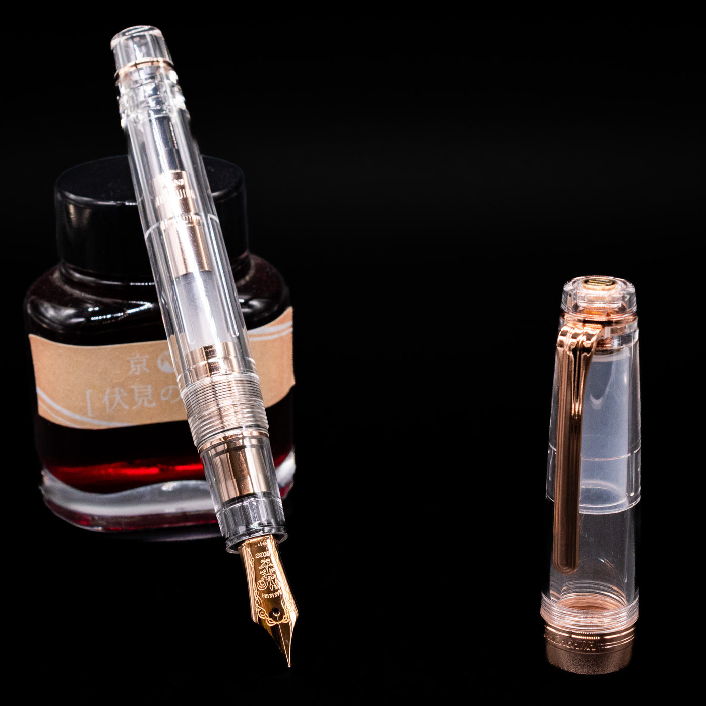 Nagasawa Original Professional Gear Fountain Pen - Skeleton Pink Gold leaning on an ink bottle uncapped showcasing the detailing on the nib.