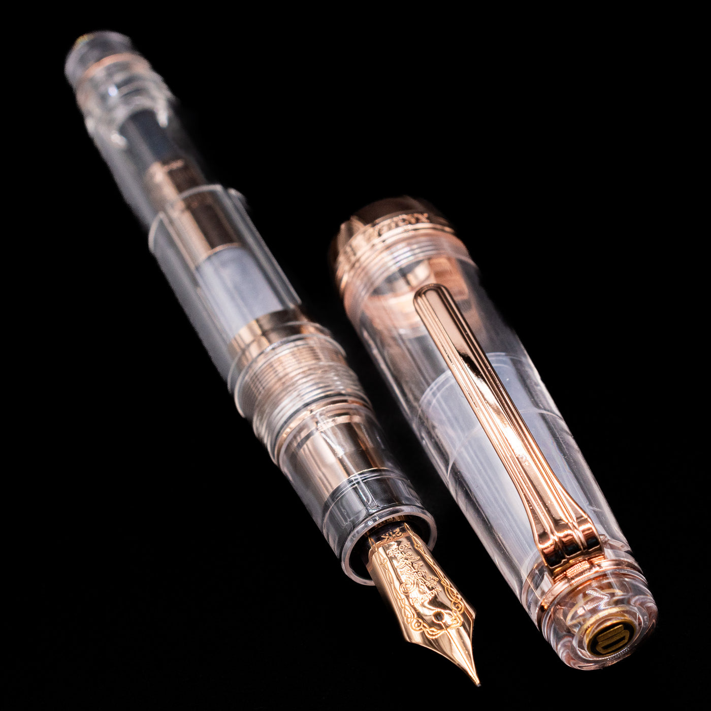 A full view of the Nagasawa Original Professional Gear Fountain Pen - Skeleton Pink Gold uncapped, with its cap laying next to the pen. 