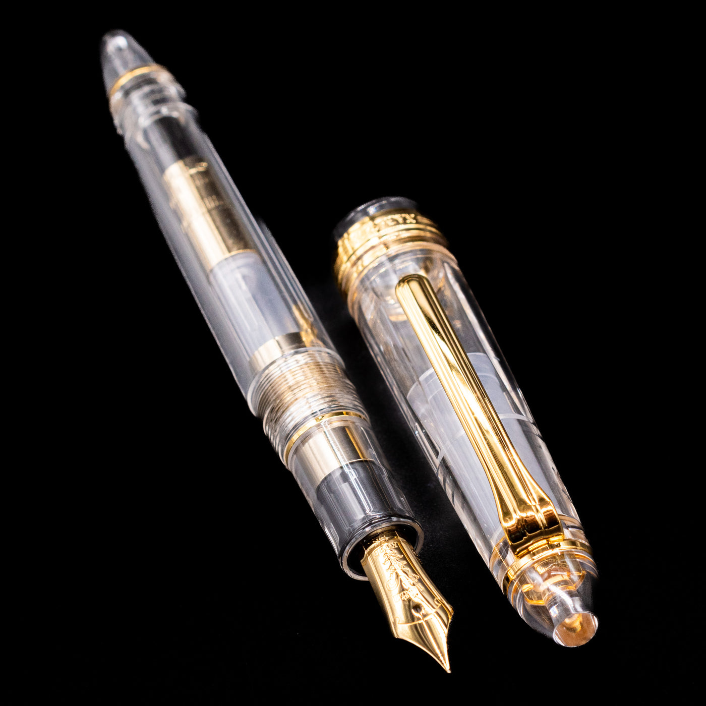 A full view of the Nagasawa Original Standard Fountain Pen - Skeleton Proske Gold uncapped, with its cap laying next to the pen. 