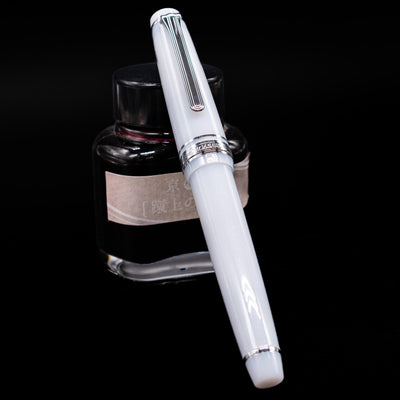 Nagasawa Original Standard Onomatopoeia Fountain Pen - Kasya Kasya capped, leaning against an ink bottle. 