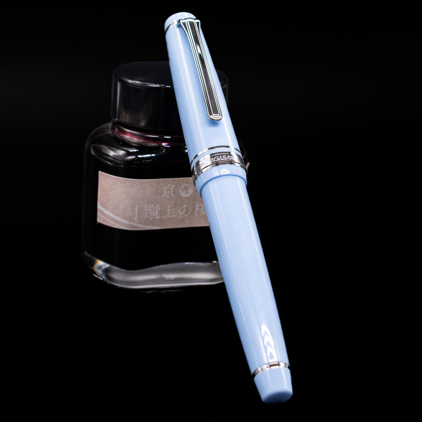 Nagasawa Original Standard Rokko Fountain Pen - Island Sky capped, leaning against an ink bottle. 