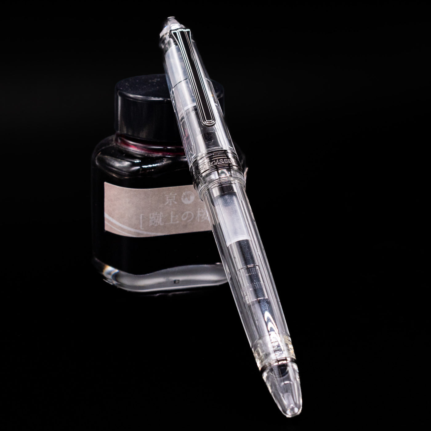 Nagasawa Original Standard Fountain Pen - Skeleton Proske Black capped, leaning against an ink bottle. 