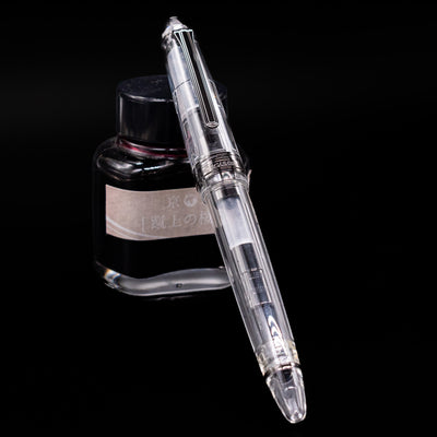 Nagasawa Original Standard Fountain Pen - Skeleton Proske Black capped, leaning against an ink bottle. 