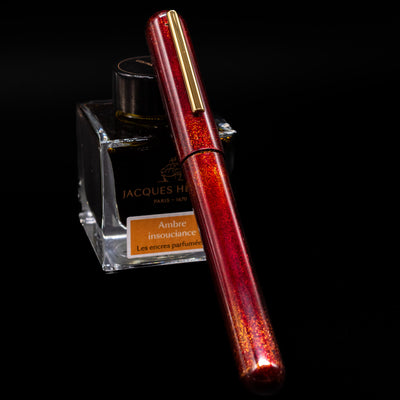 Nahvalur Ikkaku Urushi Fountain Pen - Blood Moon capped, leaning against an ink bottle. 