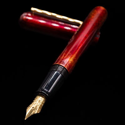 Nahvalur Ikkaku Urushi Fountain Pen - Blood Moon laying across its own cap, crossed, with a focus on the nib.
