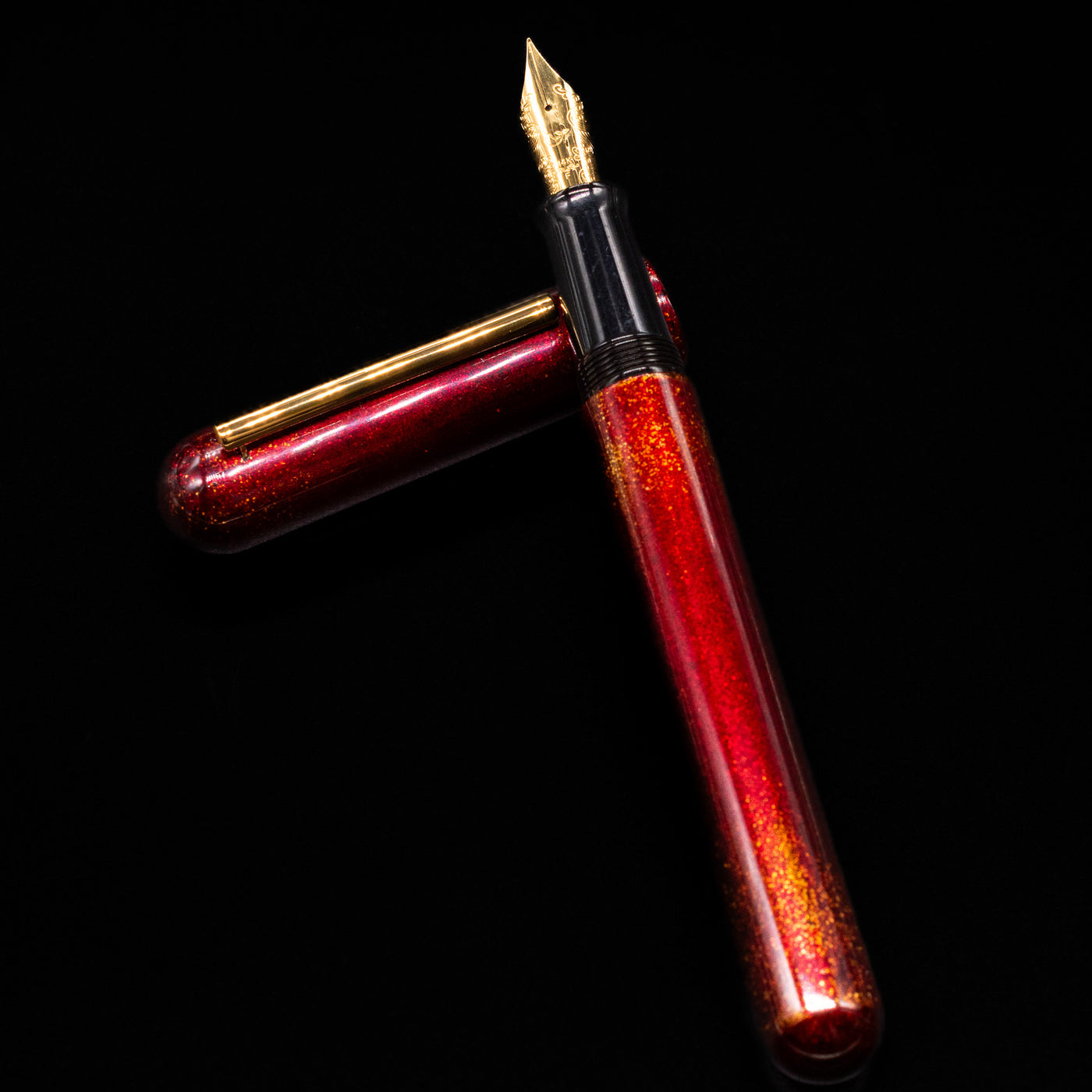 Nahvalur Ikkaku Urushi Fountain Pen - Blood Moon laying on top of its cap in a crossed position showing full view of the entire uncapped pen.