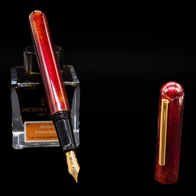 Nahvalur Ikkaku Urushi Fountain Pen - Blood Moon leaning on an ink bottle uncapped showcasing the detailing on the nib.