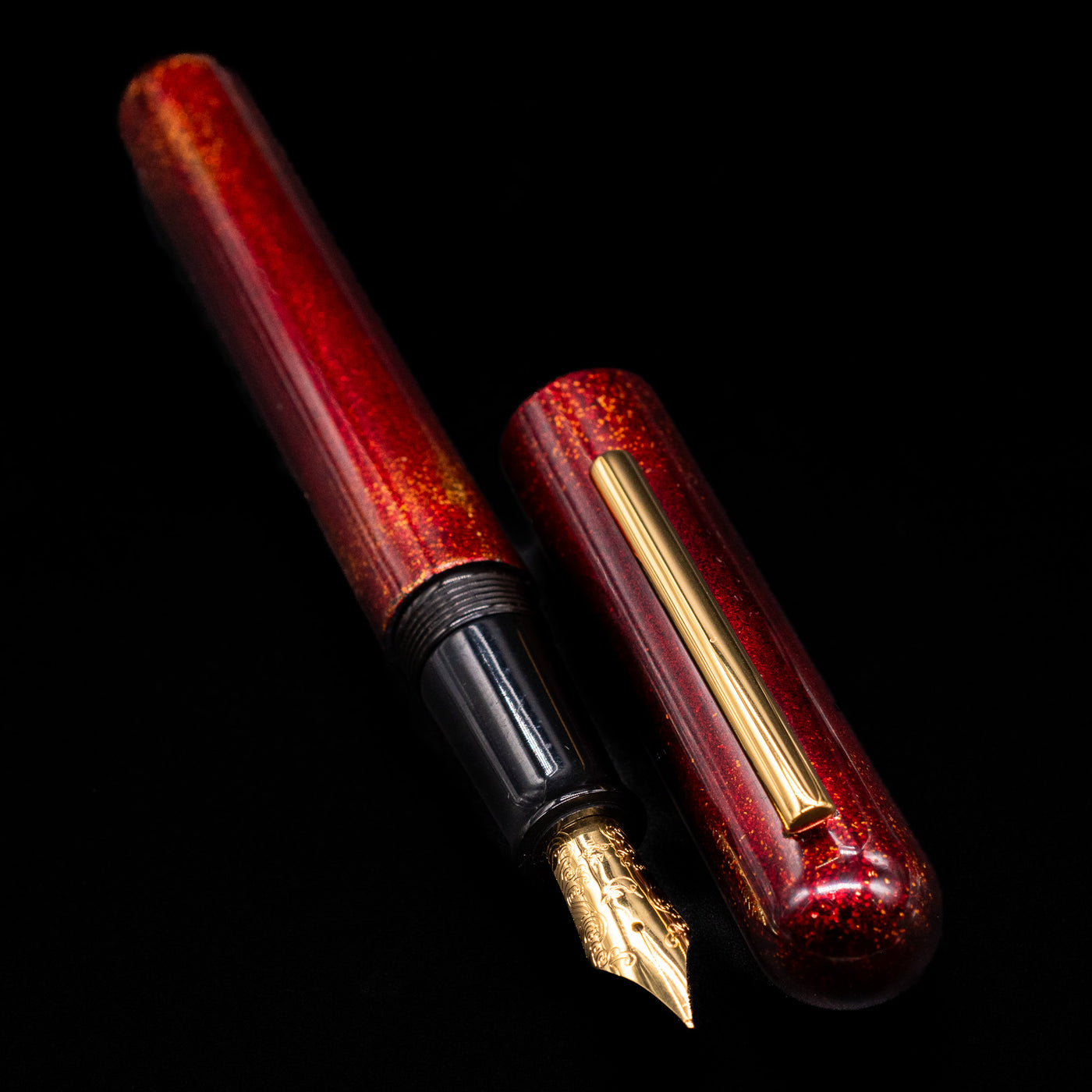 A full view of the Nahvalur Ikkaku Urushi Fountain Pen - Blood Moon uncapped, with its cap laying next to the pen. 