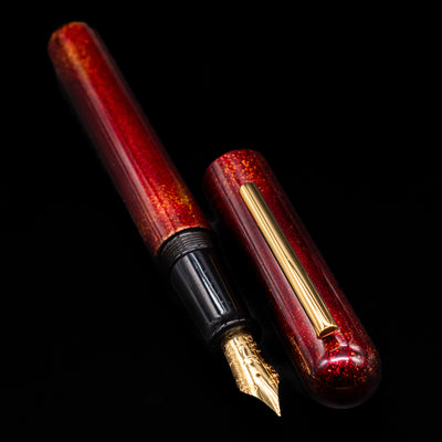 A full view of the Nahvalur Ikkaku Urushi Fountain Pen - Blood Moon uncapped, with its cap laying next to the pen. 