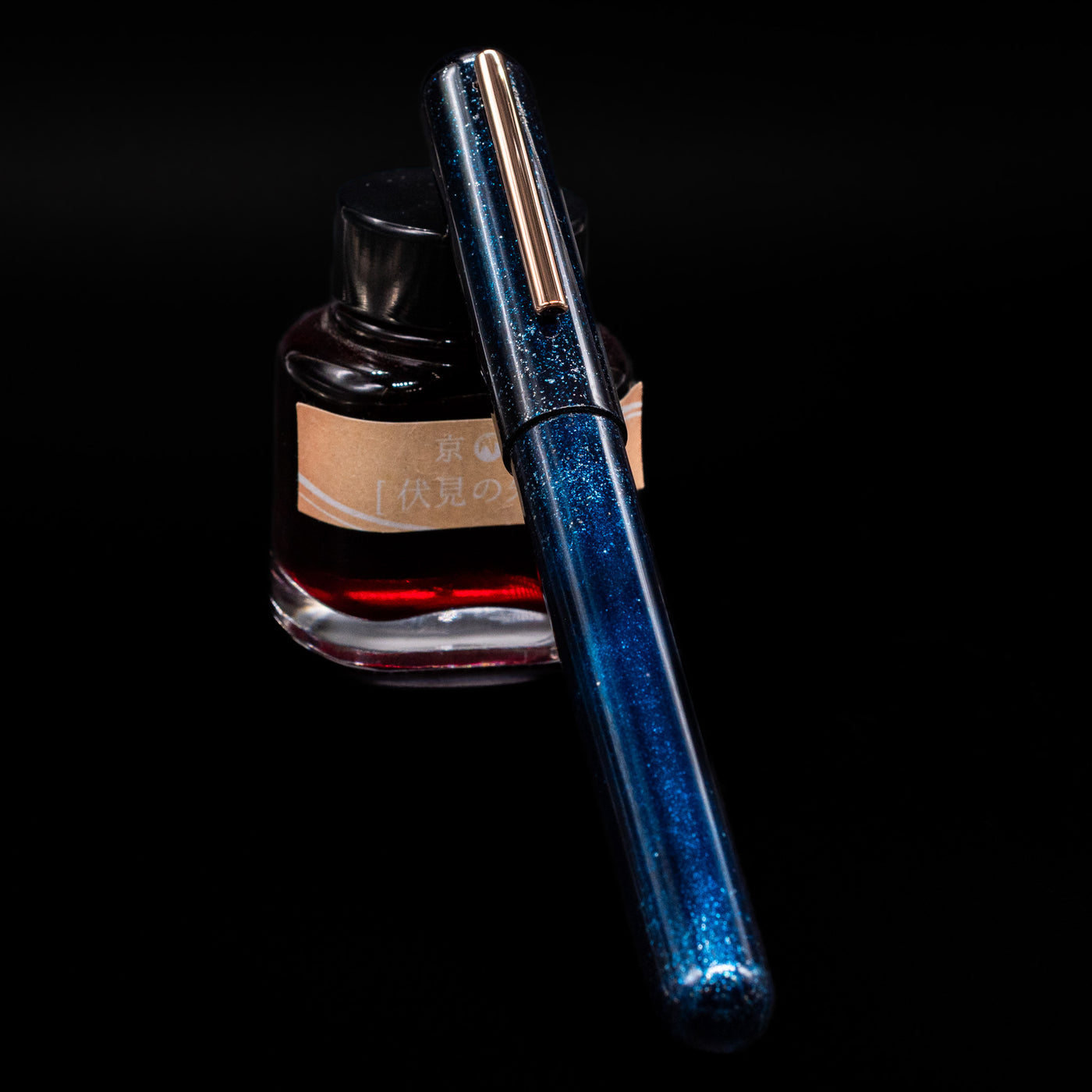 Nahvalur Ikkaku Urushi Fountain Pen - Blue Moon capped, leaning against an ink bottle. 