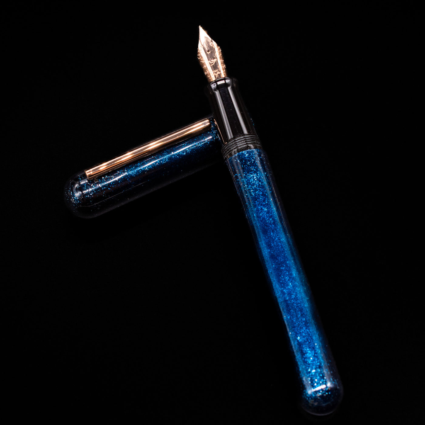 Nahvalur Ikkaku Urushi Fountain Pen - Blue Moon laying on top of its cap in a crossed position showing full view of the entire uncapped pen.