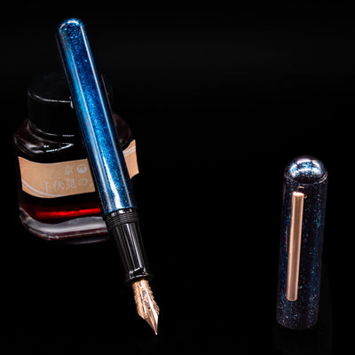 Nahvalur Ikkaku Urushi Fountain Pen - Blue Moon leaning on an ink bottle uncapped showcasing the detailing on the nib.