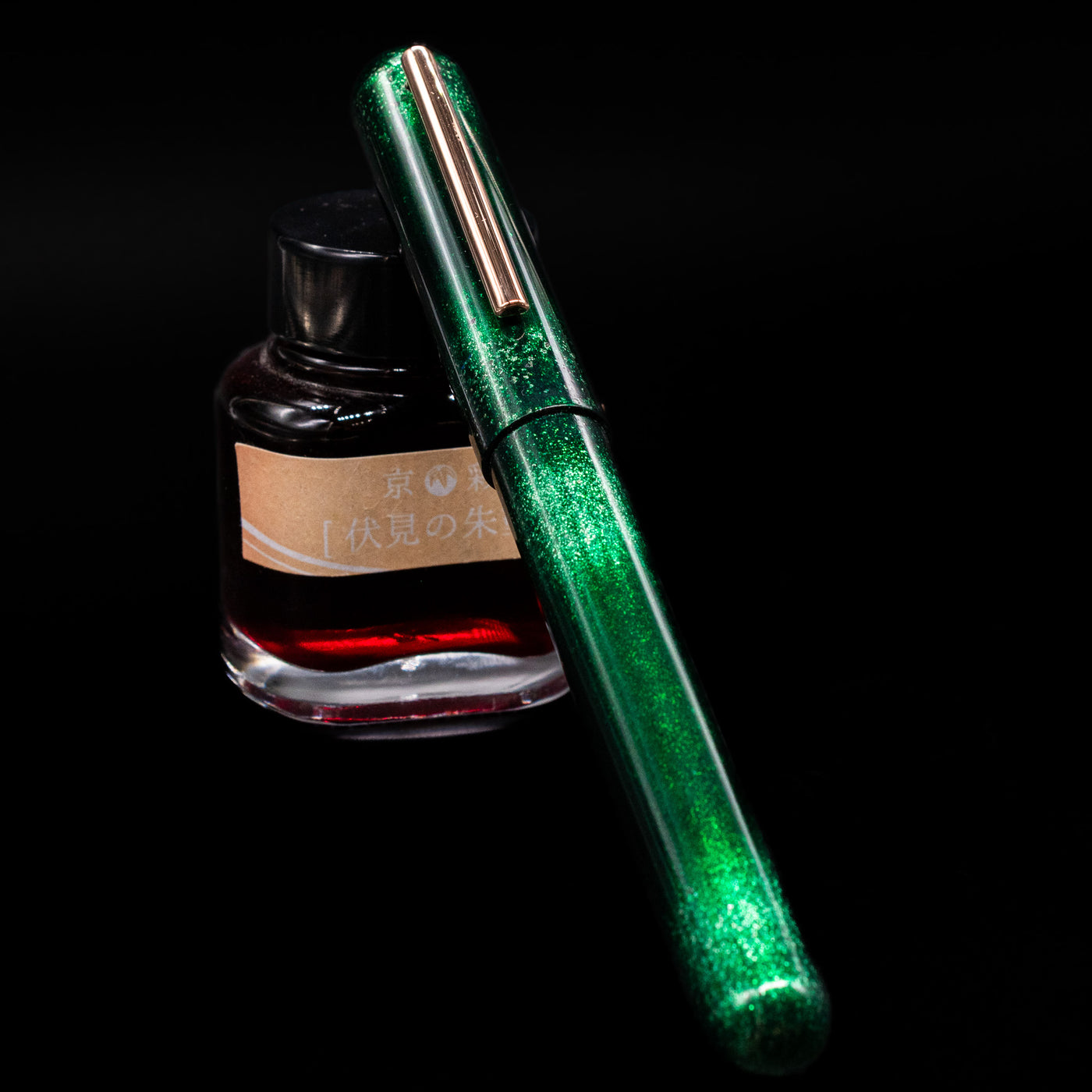 Nahvalur Ikkaku Urushi Fountain Pen - Green Moon capped, leaning against an ink bottle. 