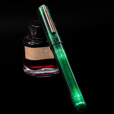 Nahvalur Ikkaku Urushi Fountain Pen - Green Moon capped, leaning against an ink bottle. 
