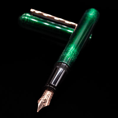 Nahvalur Ikkaku Urushi Fountain Pen - Green Moon laying across its own cap, crossed, with a focus on the nib.