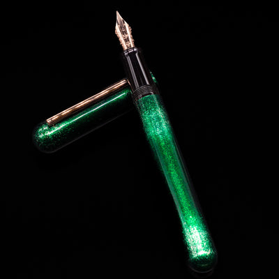 Nahvalur Ikkaku Urushi Fountain Pen - Green Moon laying on top of its cap in a crossed position showing full view of the entire uncapped pen.