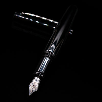 Nakaya Piccola Long Fountain Pen - Kuro Tame laying across its own cap, crossed, with a focus on the nib.