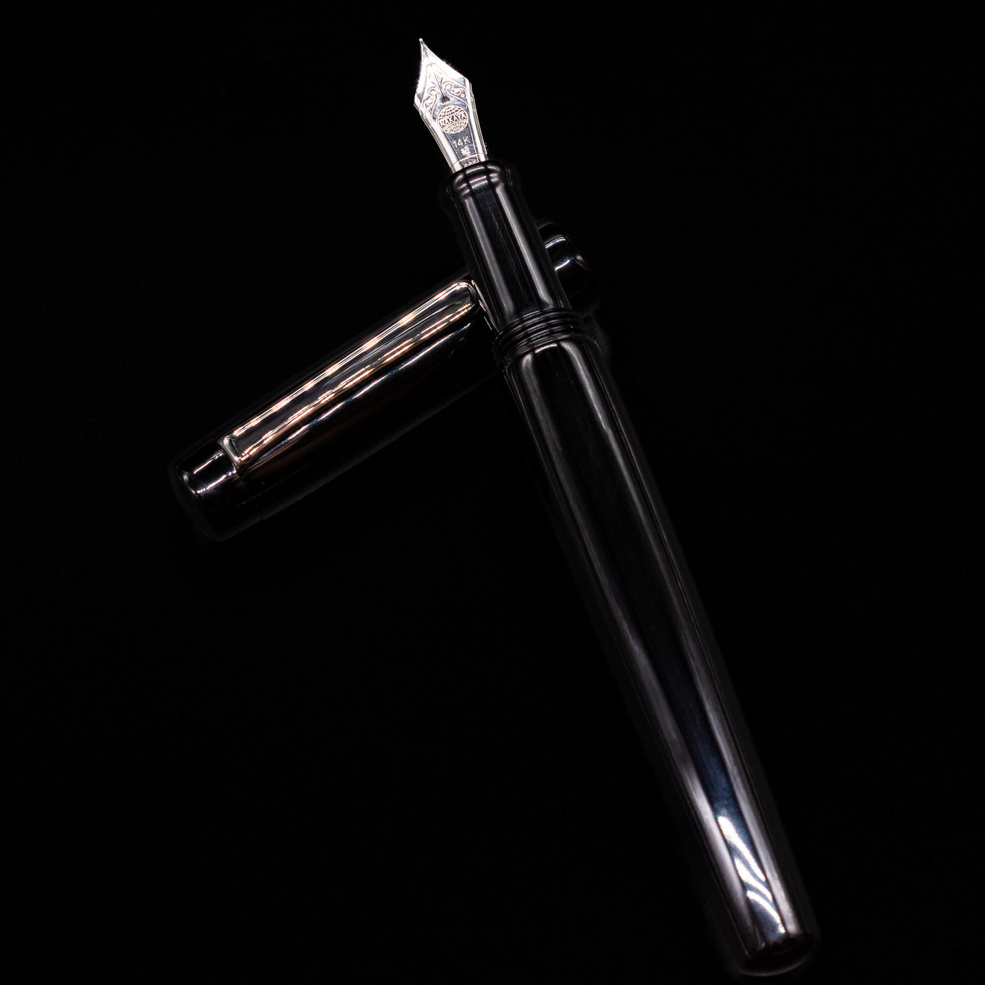 Nakaya Piccola Long Fountain Pen - Kuro Tame laying on top of its cap in a crossed position showing full view of the entire uncapped pen.