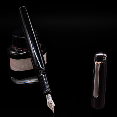 Nakaya Piccola Long Fountain Pen - Kuro Tame leaning on an ink bottle uncapped showcasing the detailing on the nib.