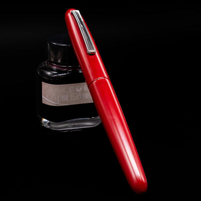 Nakaya Portable Writer Fountain Pen - AraiShu capped, leaning against an ink bottle. 