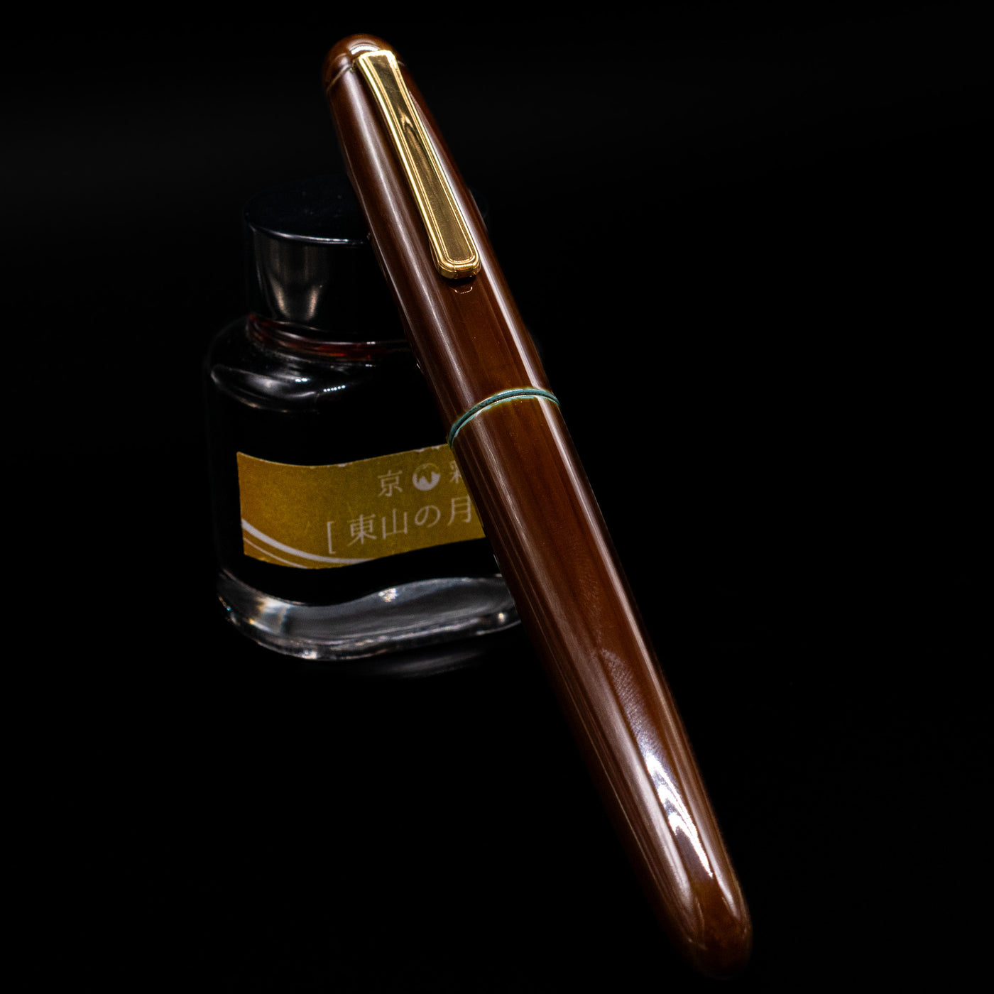 Nakaya Portable Writer Fountain Pen - Heki Tamenuri capped, leaning against an ink bottle. 
