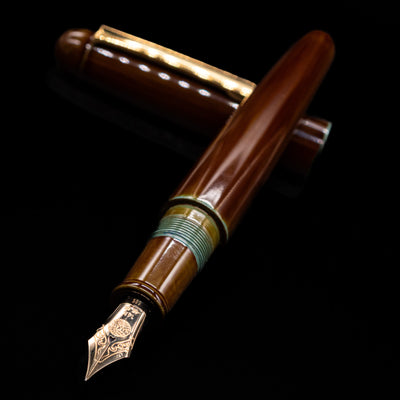 Nakaya Portable Writer Fountain Pen - Heki Tamenuri laying across its own cap, crossed, with a focus on the nib.