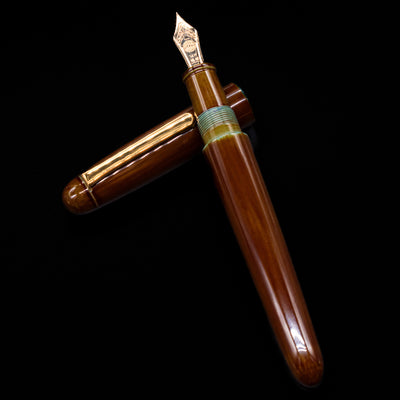 Nakaya Portable Writer Fountain Pen - Heki Tamenuri laying on top of its cap in a crossed position showing full view of the entire uncapped pen.
