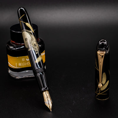 Uncapped Namiki Yukari Royale Cat fountain pen leaning on ink bottle – Showcasing detailed chinkin gold engraving and polished urushi lacquer.