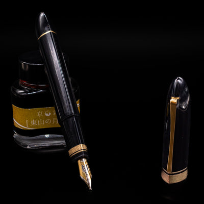 OMAS 360 Dark Blue Fountain Pen - Preowned leaning on an ink bottle uncapped showcasing the detailing on the nib.